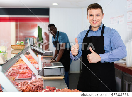 Proud male owner of butcher shop standing behind counter, giving thumbs up 47888788