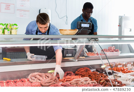 Successful owner of butcher store with his worker preparing fresh meat products for sale 47889230