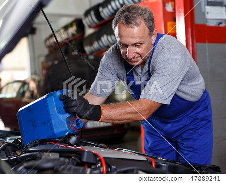 Mechanic engaged in replacement of engine oil 47889241