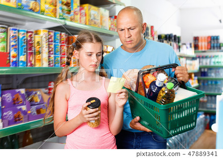 Portrait of happy family standing in supermarket with full shopping basket 47889341