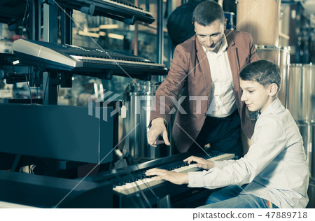 Father and teenage son examining keyboards in guitar shop 47889718