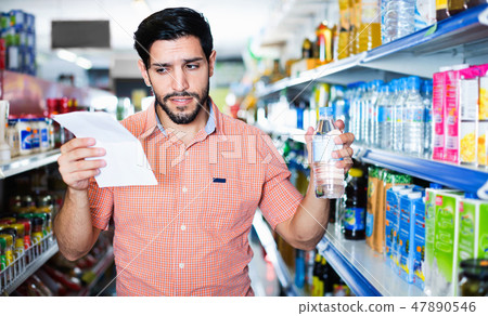 Man is choosing water with help note list in supermarket. Man is choosing water with help note list in supermarket. 47890546