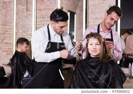 Two hairdressers making hairstyle for female client 47890602