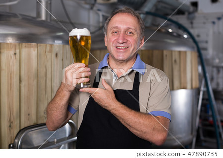 Adult brewer is standing with golden beer in glass Adult brewer is standing with golden beer in glass 47890735