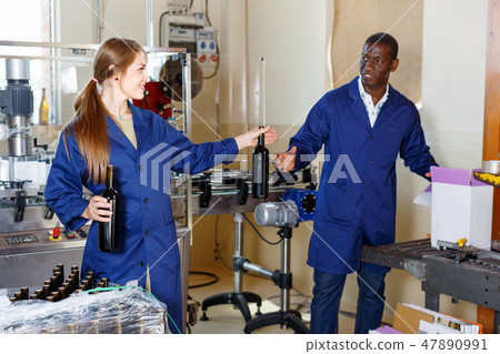 Two cheerful winery workers checking bottles with wine before packing 47890991
