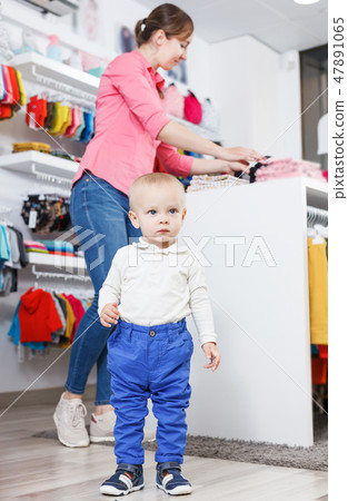 kid who is posing when his mother choosing clothes kid who is posing when his mother choosing clothes 47891065