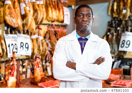 Cheerful African American seller showing thumbs up while offering delectable spanish jamon in butcher shop Cheerful African American seller showing thumbs up while offering delectable spanish jamon in butcher shop 47891103