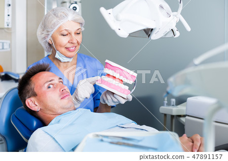 Frightened guy shocked by dental model showing by female dentist Frightened guy shocked by dental model showing by female dentist 47891157