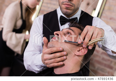 Male getting shave with straight razor in salon 47891436