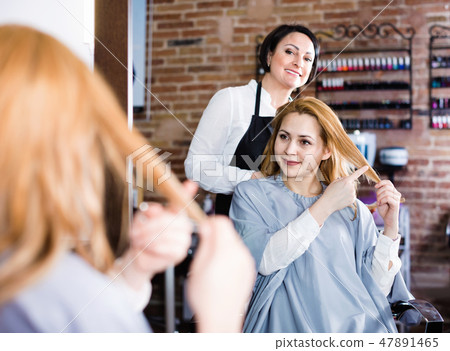 Woman points to master in hairdress salon right hair length for haircut 47891465