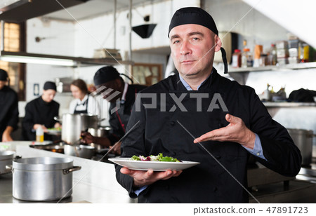 Positive male cook with cooked dish in restaurant kitchen Positive male cook with cooked dish in restaurant kitchen 47891723