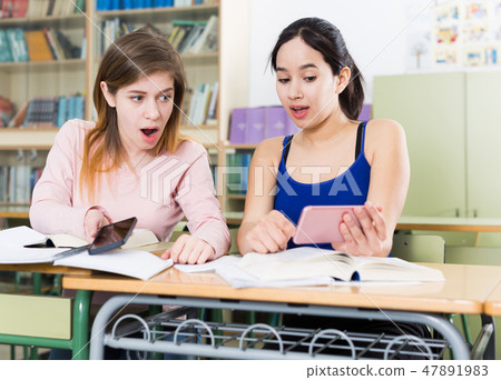 Young girls are talking about boys with phone in the classroom 47891983