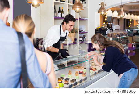 Confectioner helping customers to choose sweets Confectioner helping customers to choose sweets 47891996