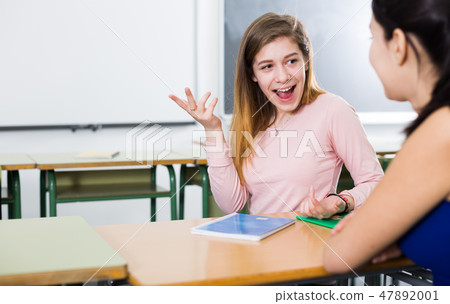 Smiling schoolgirls are talking about homework at the desk Smiling schoolgirls are talking about homework at the desk 47892001
