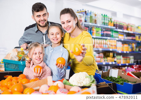 Happy family with two little girls looking for fresh oranges in supermarket Happy family with two little girls looking for fresh oranges in supermarket 47892011