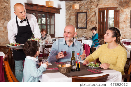 Waiter holding tray and serving family with child Waiter holding tray and serving family with child 47892012