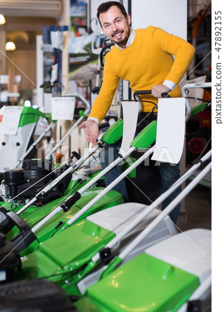 interested guy deciding on best lawnmower in garden equipment shop interested guy deciding on best lawnmower in garden equipment shop 47892155