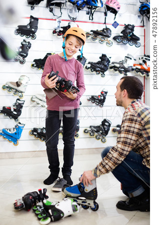male seller putting roller-skates on boy customer in sports store male seller putting roller-skates on boy customer in sports store 47892156