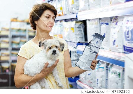 Smiling woman choosing dog food for her puppy Smiling woman choosing dog food for her puppy 47892393