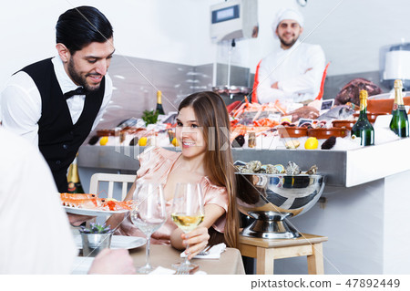 waiter bringing ordered seafood dishes to smiling couple waiter bringing ordered seafood dishes to smiling couple 47892449