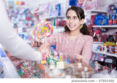 Positive small girl buying candies from seller in shop 47892480