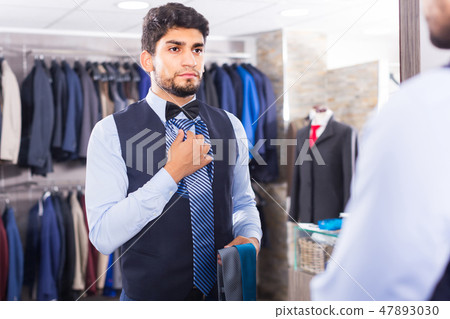 Buyer is picking up tie for waistcoat in front of the mirror Buyer is picking up tie for waistcoat in front of the mirror 47893030