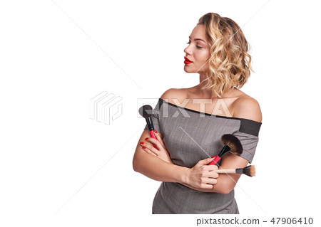Serious confident woman stylist standing with makeup brushes looking to the side 47906410