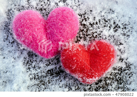 Two wool Valentines needle felted red and pink hearts lay on the snowy wooden boards 47908022