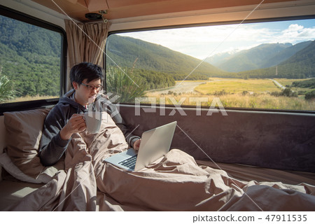 Asian man drinking coffee in camper van Asian man drinking coffee in camper van 47911535