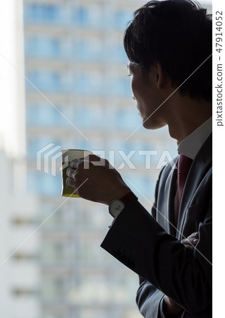 在窗口喝咖啡並且由於疲憊的工作面試放鬆工作疲勞的男性商人 在窗口喝咖啡並且由於疲憊的工作面試放鬆工作疲勞的男性商人 47914052