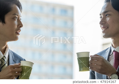 Two young businessmen resting while drinking coffee at the office corridor Two young businessmen resting while drinking coffee at the office corridor 47914167