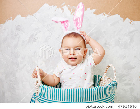Portrait of a cute baby dressed in Easter bunny ears in a basket holds egg happy easter concept Portrait of a cute baby dressed in Easter bunny ears in a basket holds egg happy easter concept 47914686