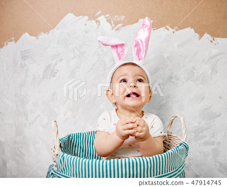 Portrait of a cute baby dressed in Easter bunny ears in a basket holds egg happy easter concept Portrait of a cute baby dressed in Easter bunny ears in a basket holds egg happy easter concept 47914745