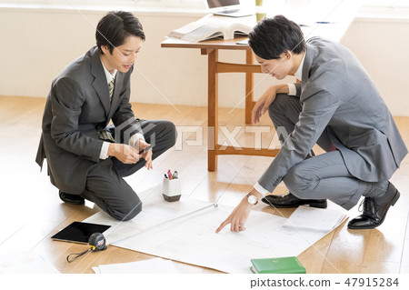 Seniors who squat down on the floor of the office and check the architectural drawing and two junior male businessmen 47915284