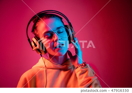 Fashion pretty woman with headphones listening to music over neon background Fashion pretty woman with headphones listening to music over neon background 47916330