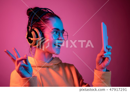 Fashion pretty woman with headphones listening to music over neon background Fashion pretty woman with headphones listening to music over neon background 47917291