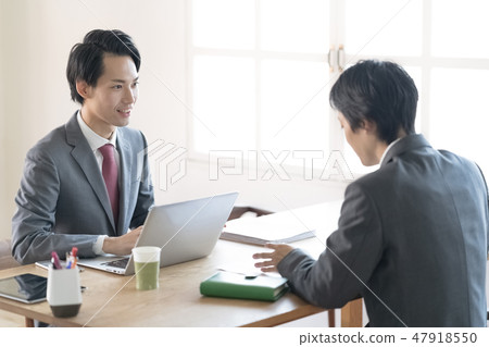 Two young men businessmen meeting at a bright window side seat Two young men businessmen meeting at a bright window side seat 47918550
