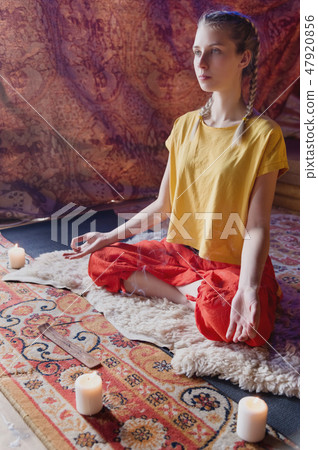 Portrait of a young girl in bright clothes practicing meditation in a crafting room surrounded by 47920856