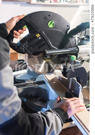 Close up of hands by profession a carpenter cuts wooden boards with a circular saw on a workbench Close up of hands by profession a carpenter cuts wooden boards with a circular saw on a workbench 47920866