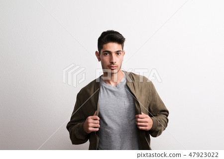 A confident young hispanic man in a studio, holding jacket. 47923022