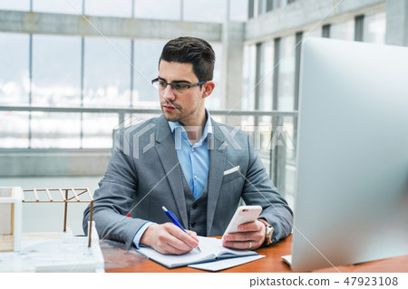 Young businessman or architect with computer and smartphone in office, working. Young businessman or architect with computer and smartphone in office, working. 47923108