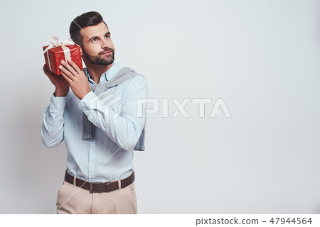 What is inside? Attractive stylish man is holding a gift box near his ear and trying to guess what What is inside? Attractive stylish man is holding a gift box near his ear and trying to guess what 47944564