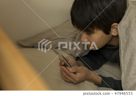 在床上睡覺昏昏欲睡的初中生高中生使用智能手機的男孩 47946555