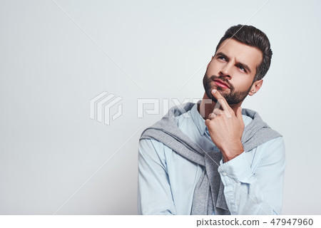 Thinking about the future...Close-up studio portrait of young bearded man keeping hand on chin Thinking about the future...Close-up studio portrait of young bearded man keeping hand on chin 47947960