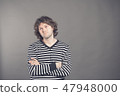 Studio shot of pensive young European male with voluminous hair posing at blank wall, keeping arms 47948000