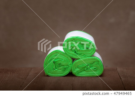 Three roll green eco garbage bag end view isolated on brown wooden background. 47949465
