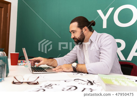 Dark-haired bearded man in a white t-shirt checking information online 47950475