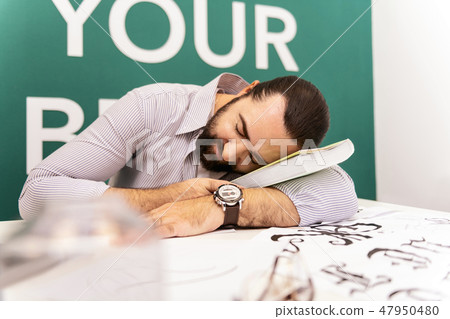 Dark-haired bearded man in a white t-shirt napping in the classroom Dark-haired bearded man in a white t-shirt napping in the classroom 47950480