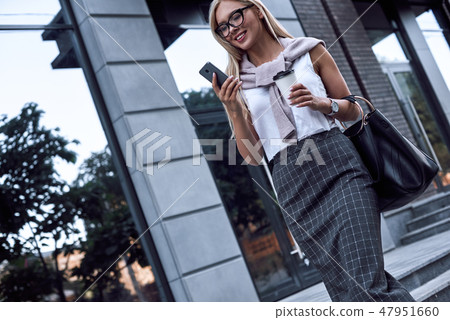 Young stylish woman chatting at smartphone. She walks with morning coffee Young stylish woman chatting at smartphone. She walks with morning coffee 47951660
