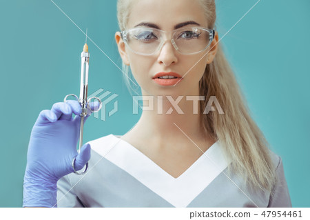 Beautiful young doctor in medical robe holding syringe with liquid. Isolated over blue background, 47954461